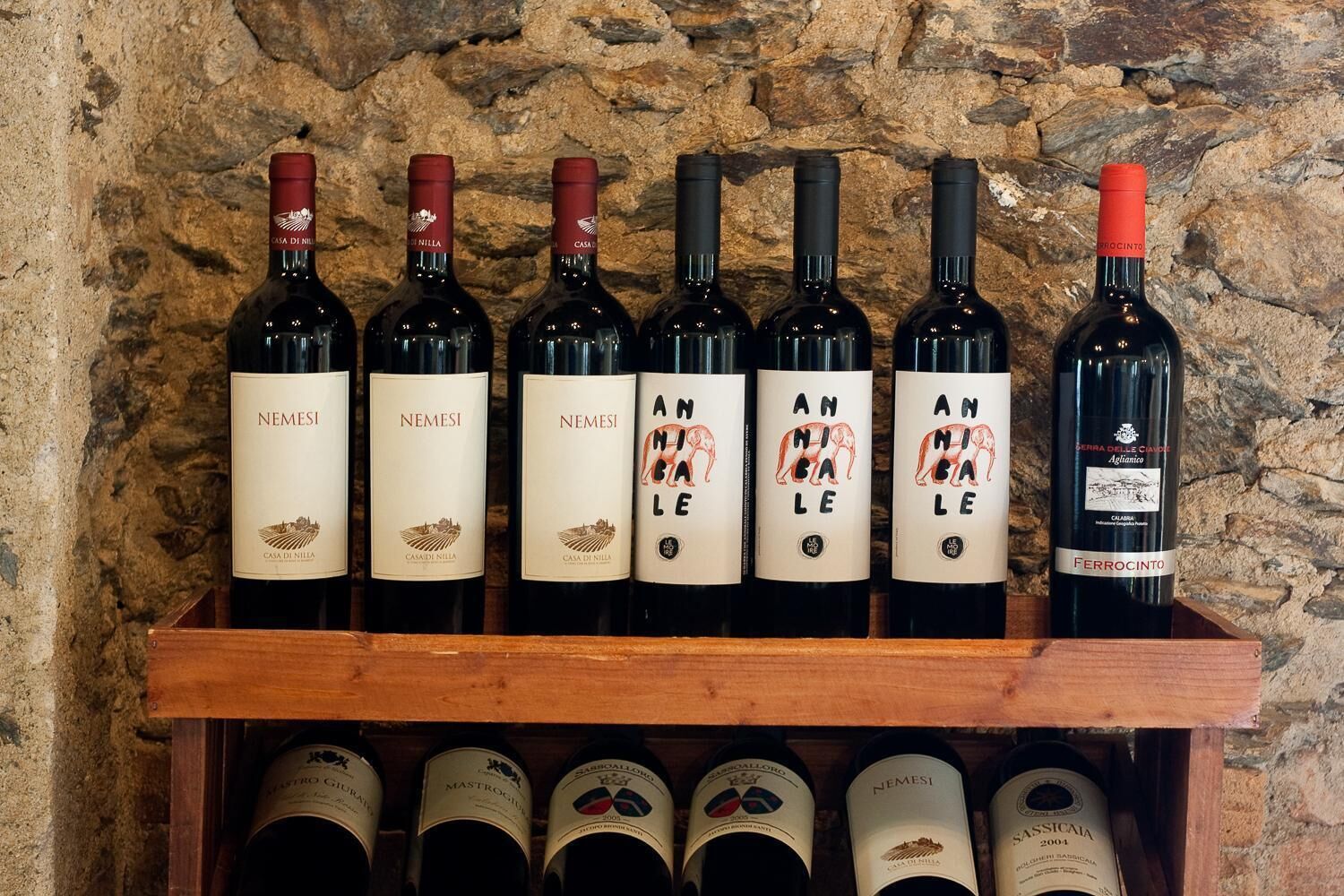 A wooden wine rack holding several wine bottles against a stone wall background.