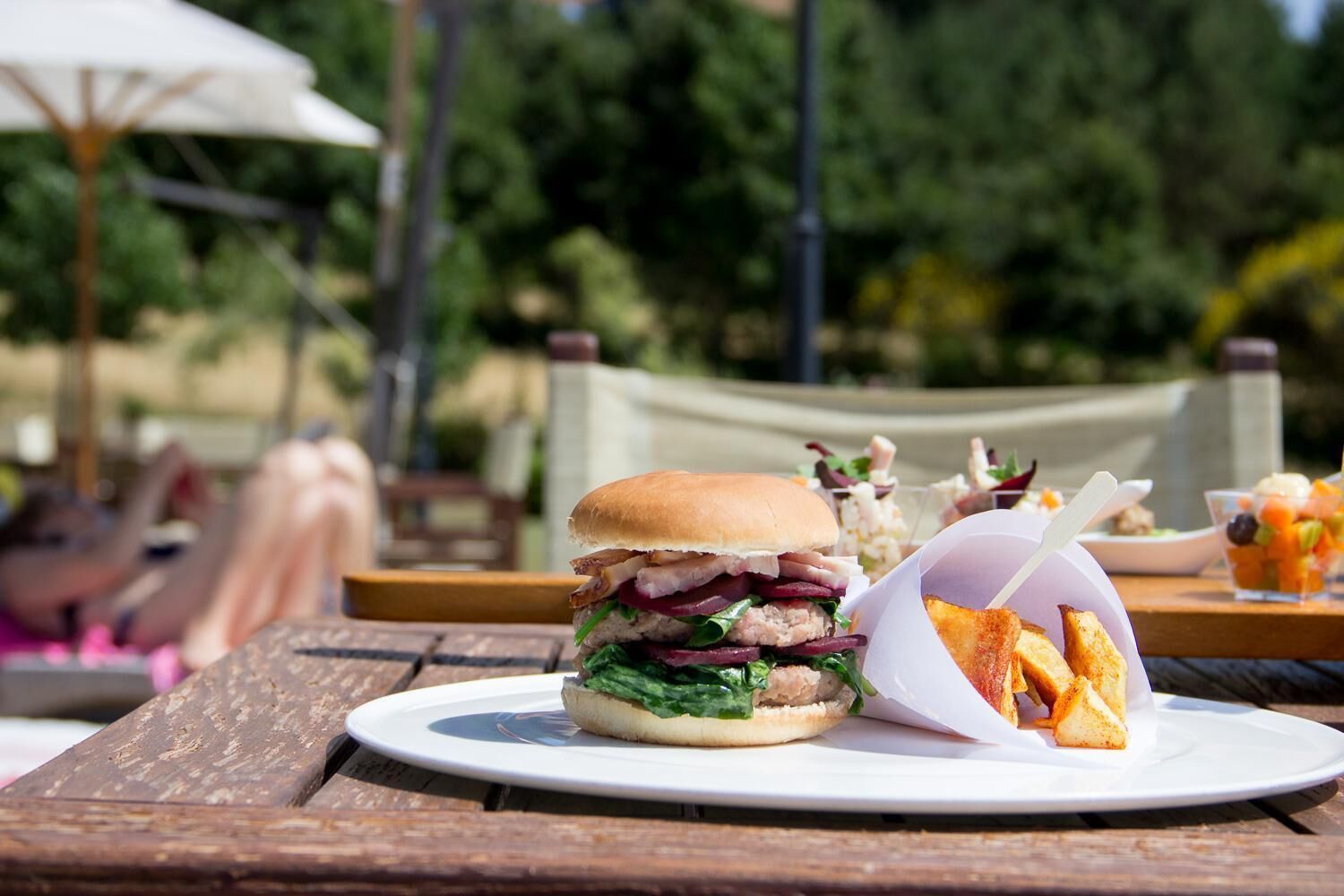 A burger with fries on a wooden table outdoors.
