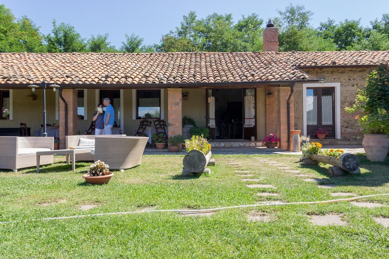 A rustic house with a tiled roof, outdoor seating, and potted plants.