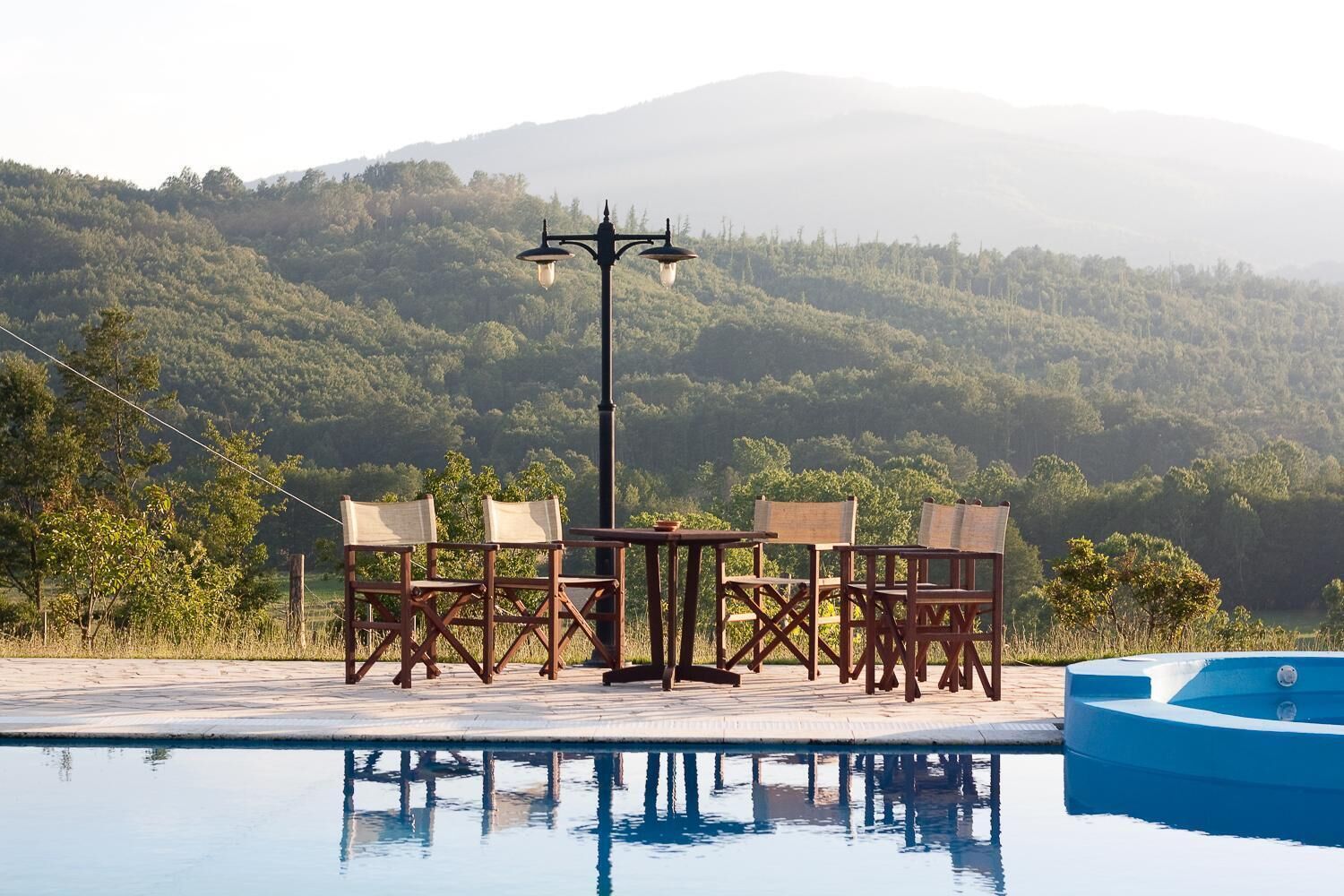 Un espace aménagé au bord de la piscine, avec une table et des chaises, un lampadaire et une vue sur une chaîne de montagnes boisées.