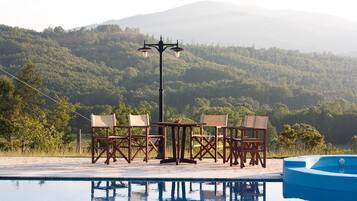 Un espace aménagé au bord de la piscine, avec une table et des chaises, un lampadaire et une vue sur une chaîne de montagnes boisées.