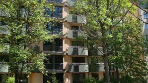 Een meerlaags woongebouw met balkons, omgeven door bomen en groen.
