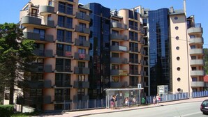 Een meerlaags appartementencomplex met balkons, een bushalte en een voetpad.