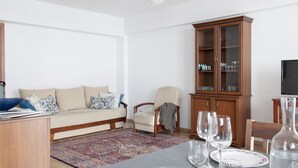 Een woonkamer met een bank, fauteuil, houten kast en een eettafel gedekt met glazen en borden.