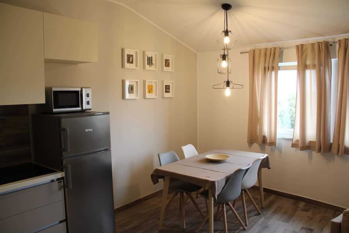 A compact kitchen with a microwave and refrigerator, a dining table with chairs, and a window with curtains.