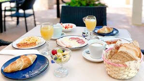 Mesa de comedor al aire libre con artículos de desayuno como cruasanes, fruta y jugo.