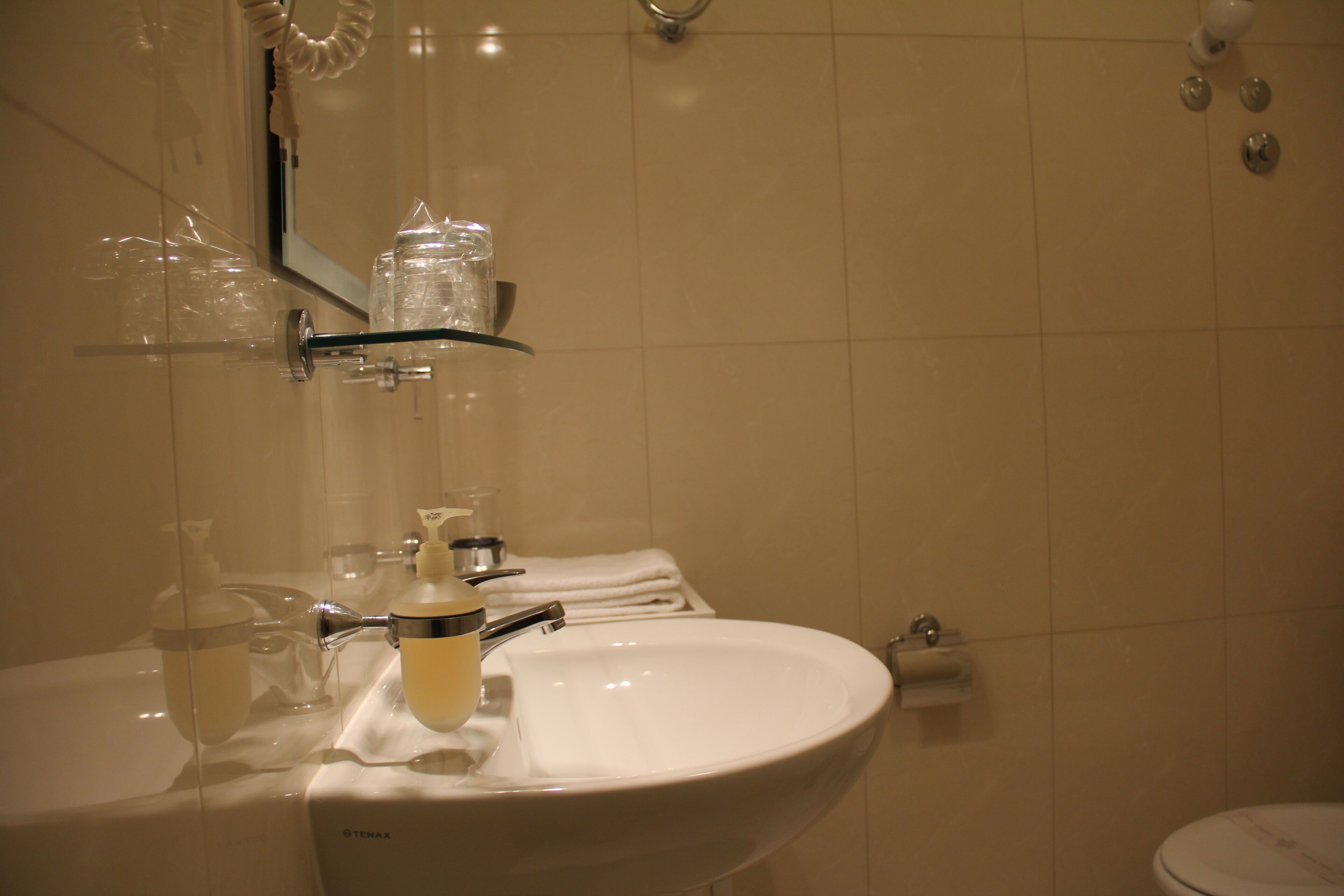 A bathroom with a white sink, a mirror, and a glass shelf holding toiletries.