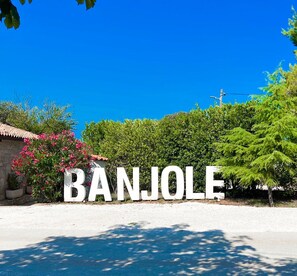 Une enseigne avec le mot « BANJOLE » écrit en grandes lettres blanches, entourée de verdure et se dressant sous un ciel bleu clair.