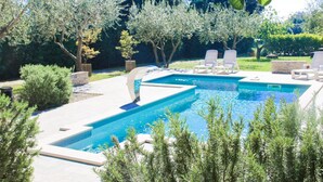 Una piscina rectangular con solárium empedrado y sillones de descanso alrededor.