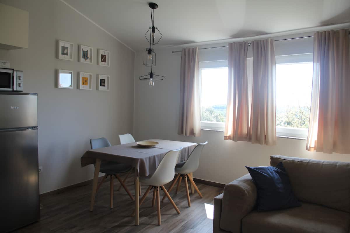 A compact living space with a dining area, a sofa, a refrigerator, and a window with curtains.