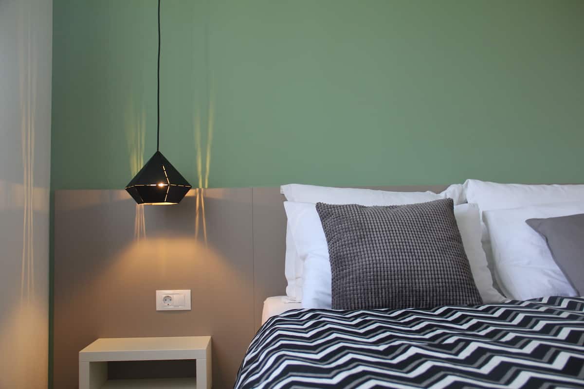A bedroom with a bed, a bedside table, and a hanging light fixture.