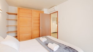 A bedroom with a bed, a wooden wardrobe, and a bathroom visible through an open door.