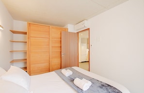 A hotel room with a bed, a wooden wardrobe, a built-in shelf, and a bathroom visible through an open door.