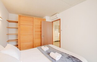 Un dormitorio con cama, un armario de madera y un baño visible a través de una puerta abierta.