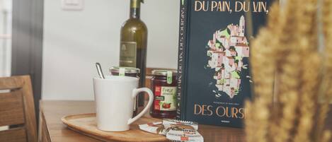 A table with a white mug, a bottle of wine, a book titled 'DU PAI, DU VIN, DES OURS', and a packet of biscuits.