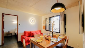 A dining area with a wooden table set for four, a red sofa, and a window with curtains.