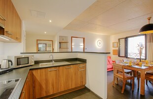 Una cocina moderna con armarios de madera, microondas integrado y un comedor con mesa y sillas de madera.
