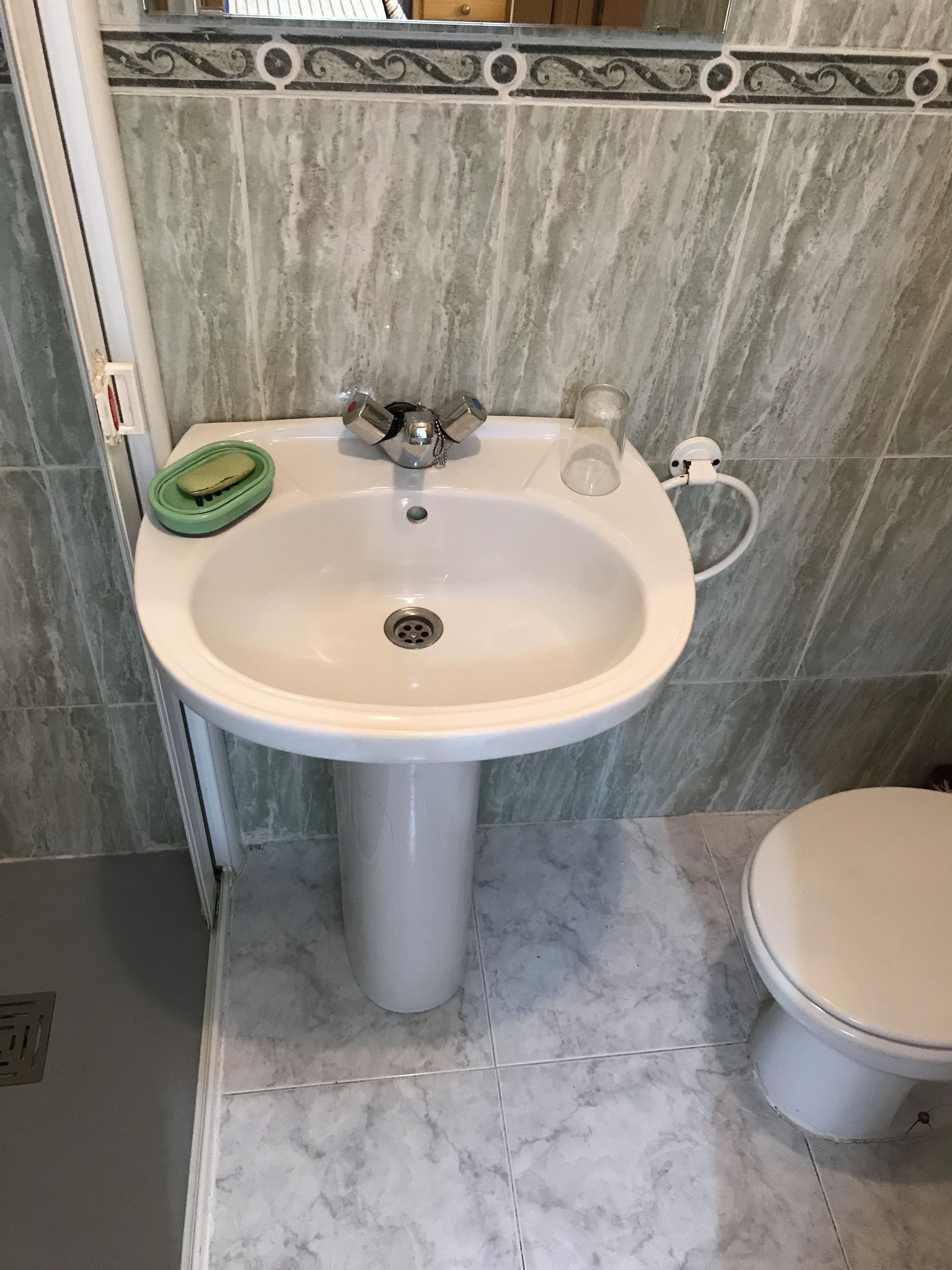 A bathroom with a white pedestal sink, a green soap dish, and a toilet.