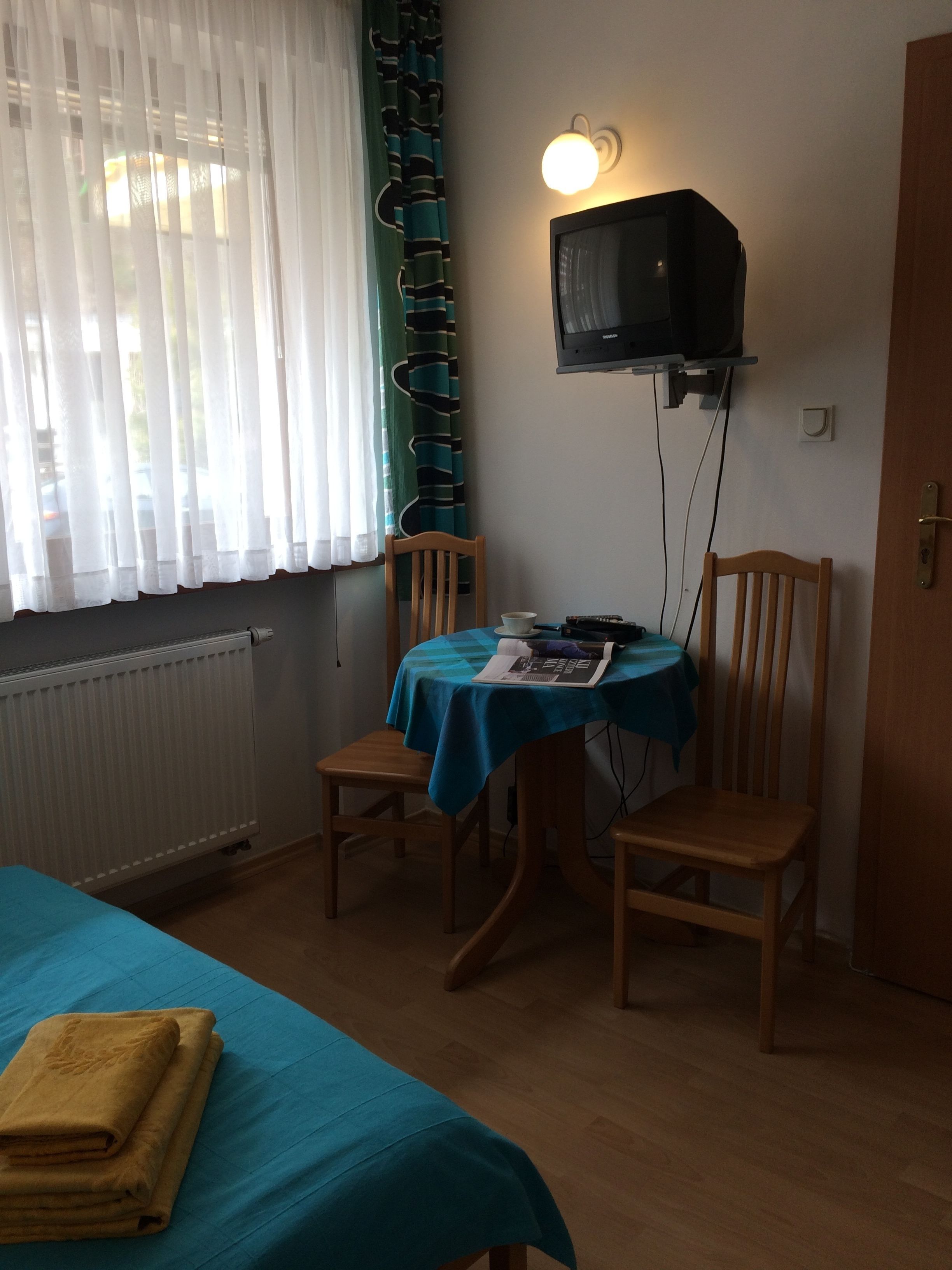 Una habitación con cama, una mesa y sillas, televisión y ventana con cortinas.