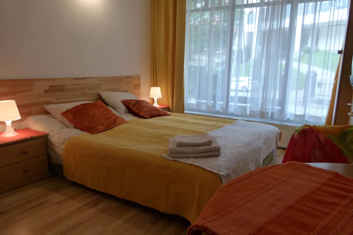Een slaapkamer met een houten hoofdeinde, twee bedlampen, een bed met een gele sprei, twee kussens en een raam met gordijnen.