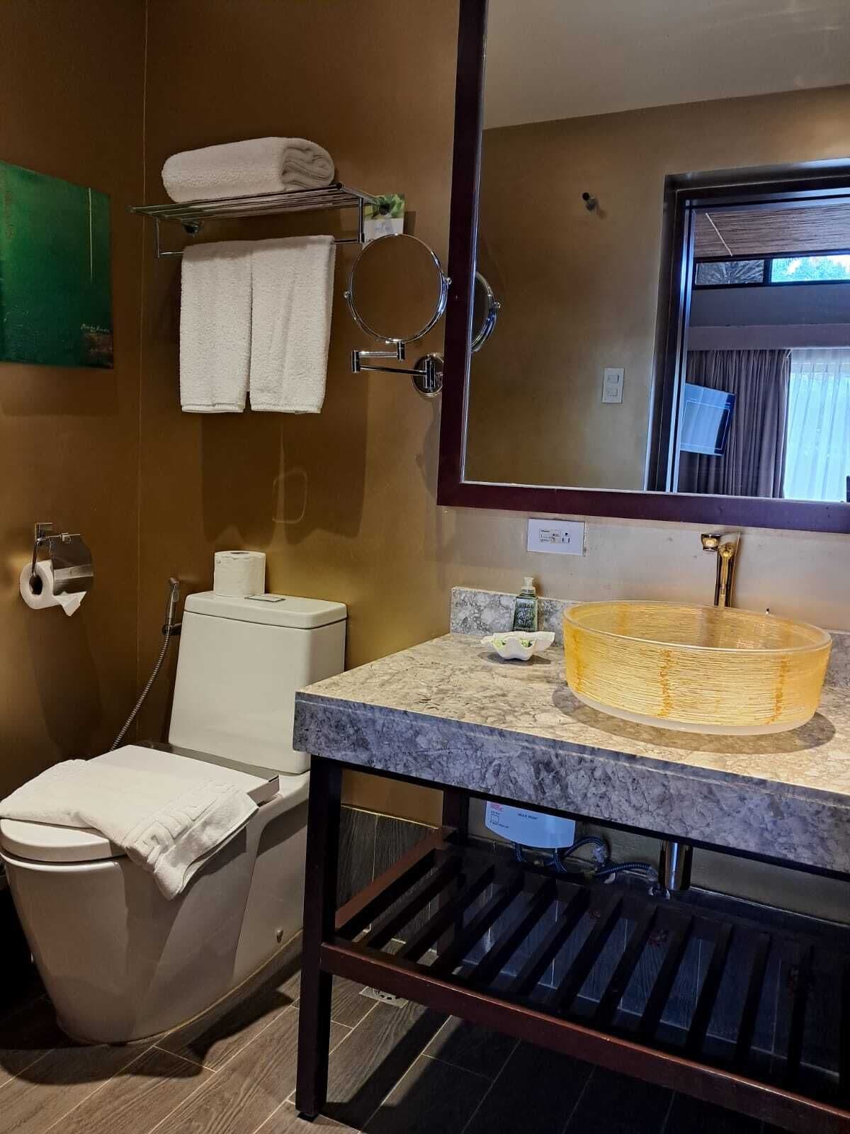 Un baño con lavamanos de mármol, inodoro, toallero y espejo.