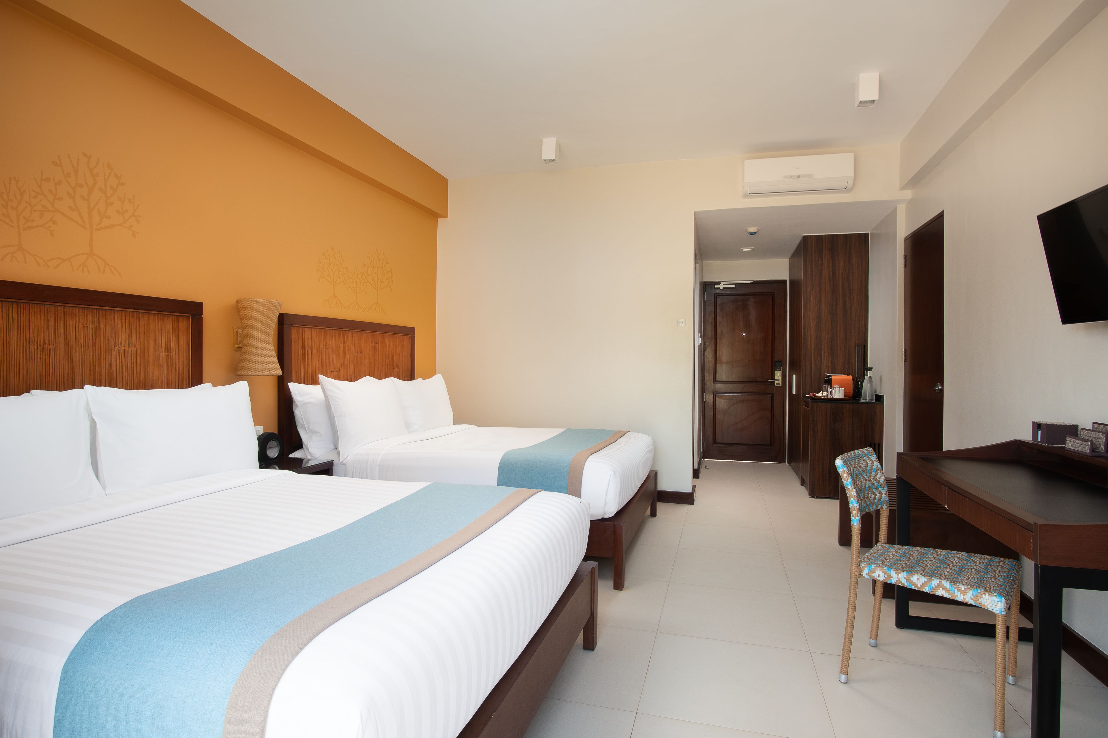 Habitación de hotel con dos camas, un escritorio, una silla, un televisor y una puerta que da a un baño.