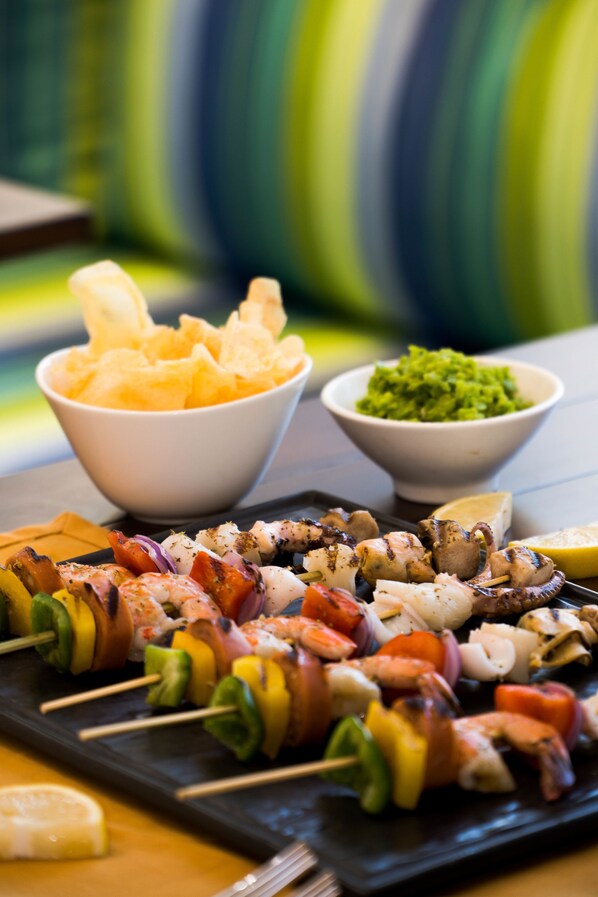 Grillede grøntsags- og fiskespyd, en skål chips og en skål guacamole.