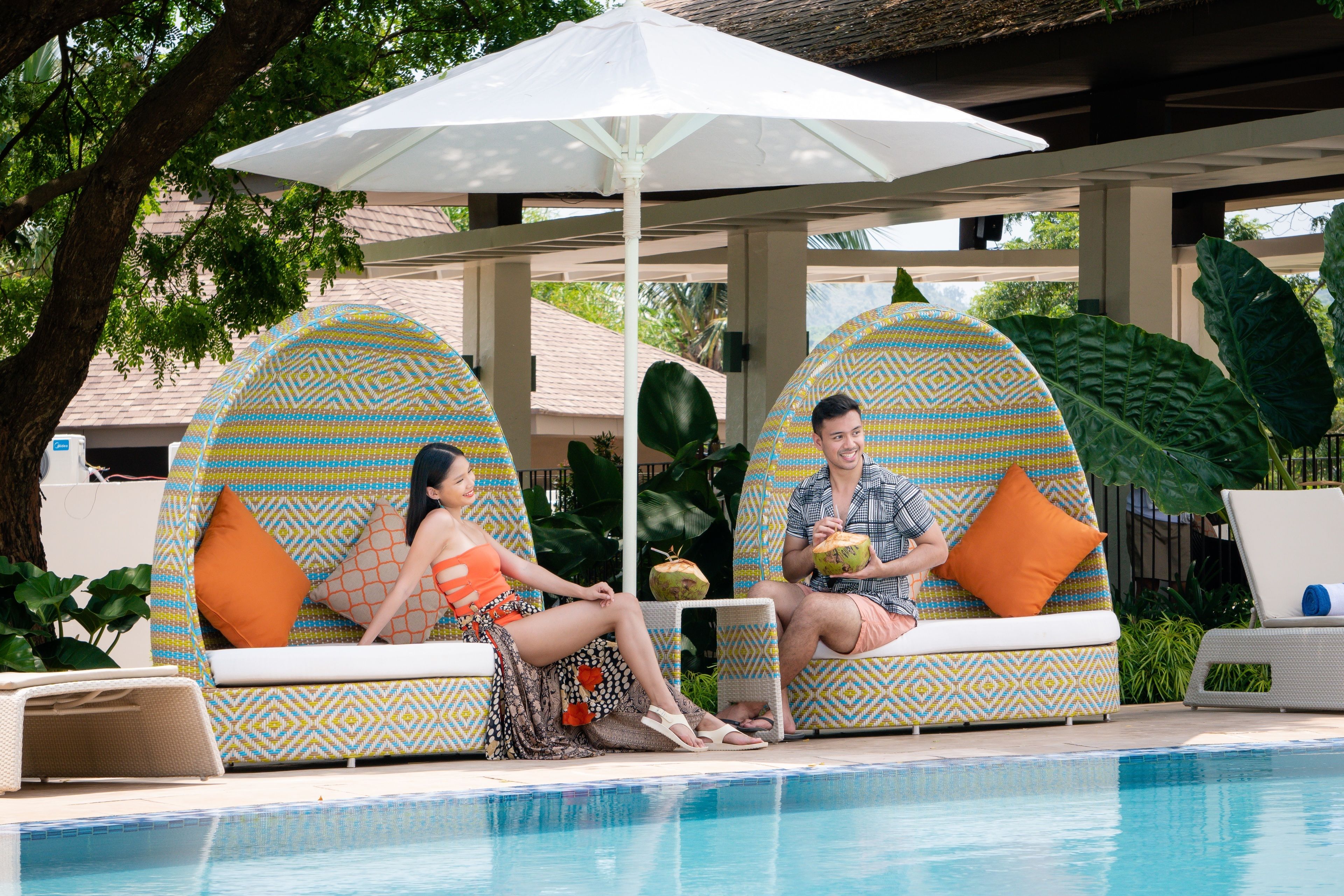 A poolside area with two patterned lounge chairs, a white umbrella, and a pool.