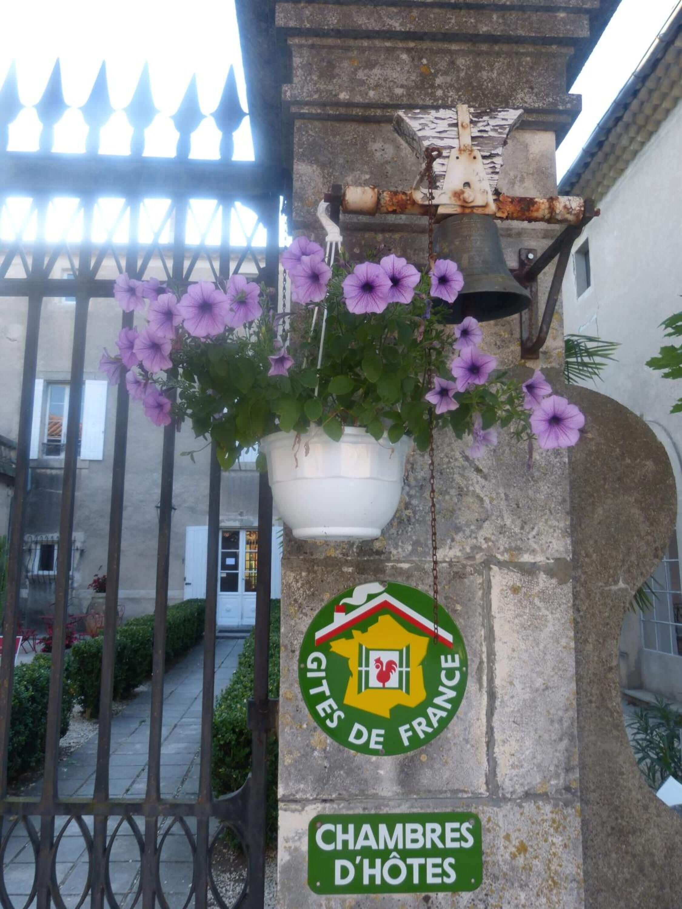 Un pilar de piedra con un letrero que dice “Chambres D'Hotes” y una maceta con flores moradas.