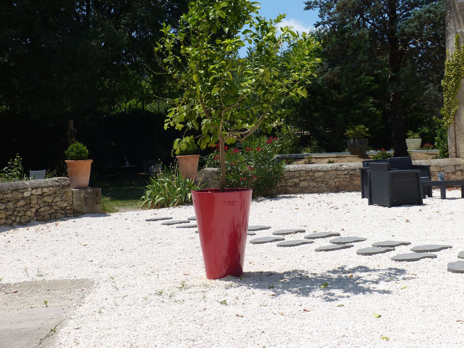 A garden area with a red planter, stone wall, and outdoor furniture.