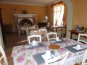 A dining area with a brick fireplace, floral tablecloths, and white chairs.