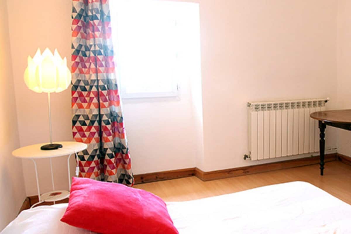 Un dormitorio con cama, mesita de noche, lámpara, radiador y cómoda.