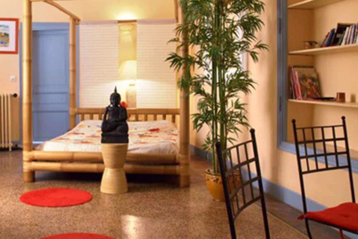 Una habitación con una cama, una silla, una lámpara, una estantería y una planta en maceta.