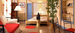 A room with a bed, a chair, a lamp, a bookshelf, and a potted plant.