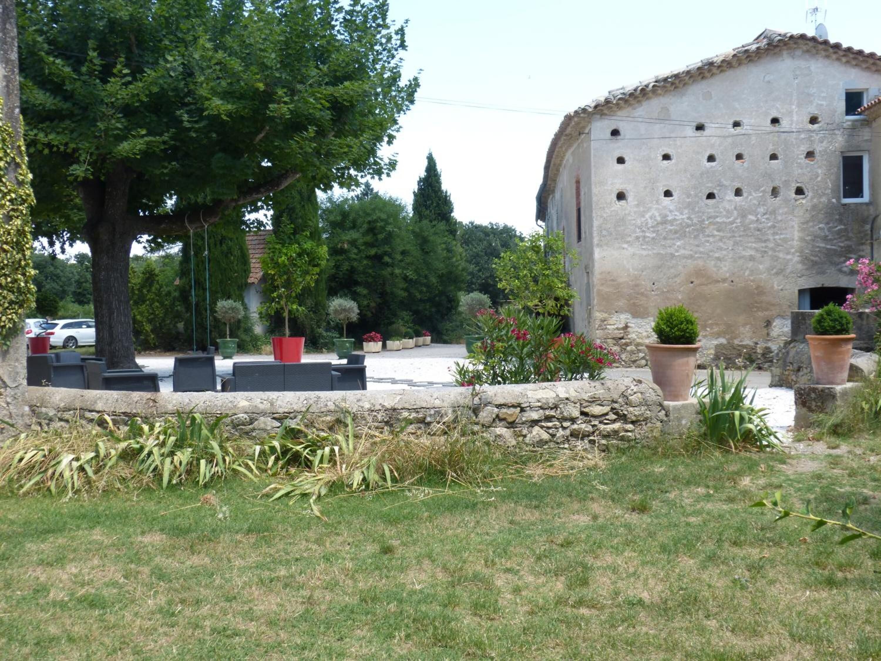 A rustic stone building with a tiled roof, surrounded by a garden with potted plants and a lawn.