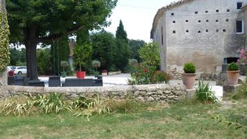 A rustic stone building with a tiled roof, surrounded by a garden with potted plants and a lawn.