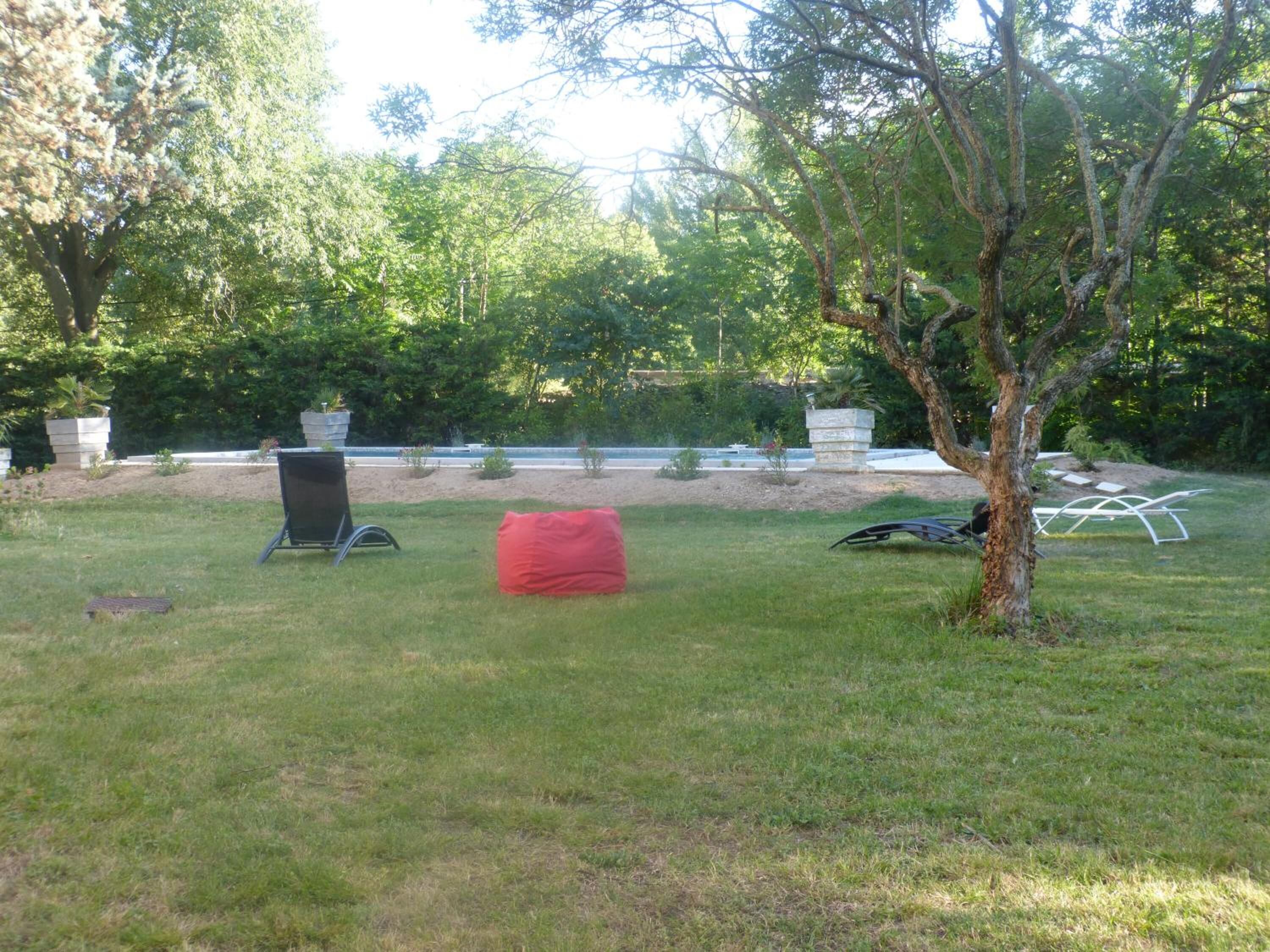 Un espacio al aire libre con césped, un sillón de tumba tipo alforfón rojo, una silla de metal negra y una silla de metal blanca.