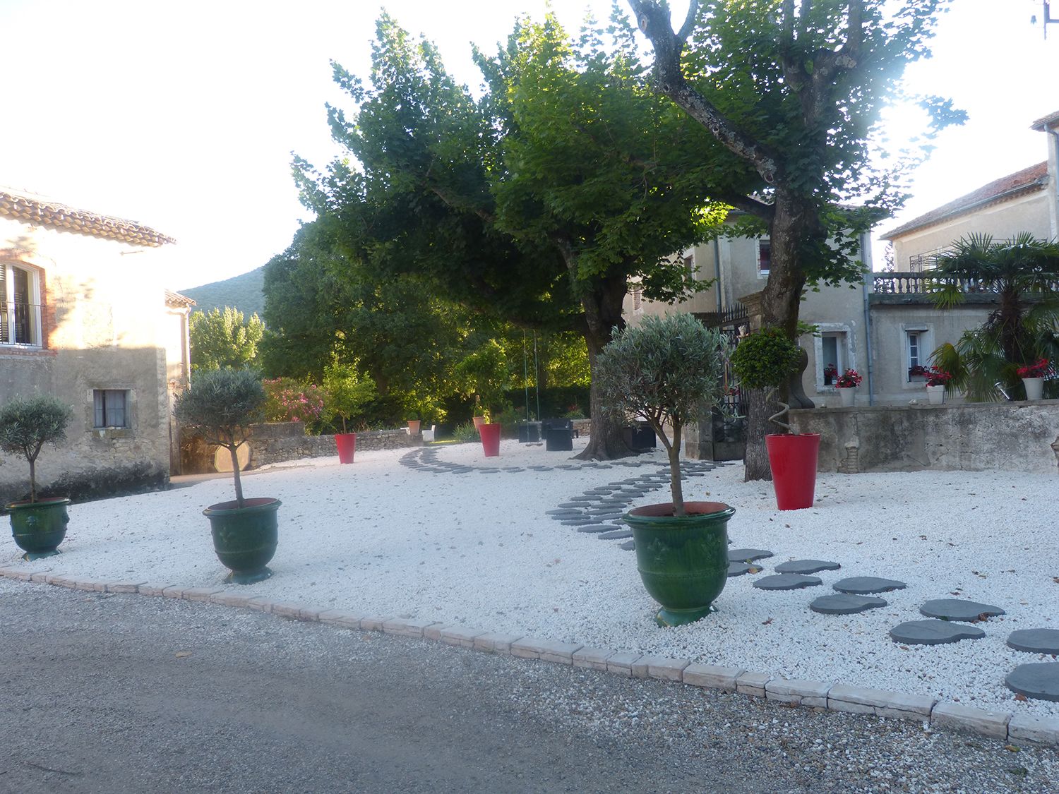 Un patio con plantas en macetas, un camino de grava y un muro de piedra.