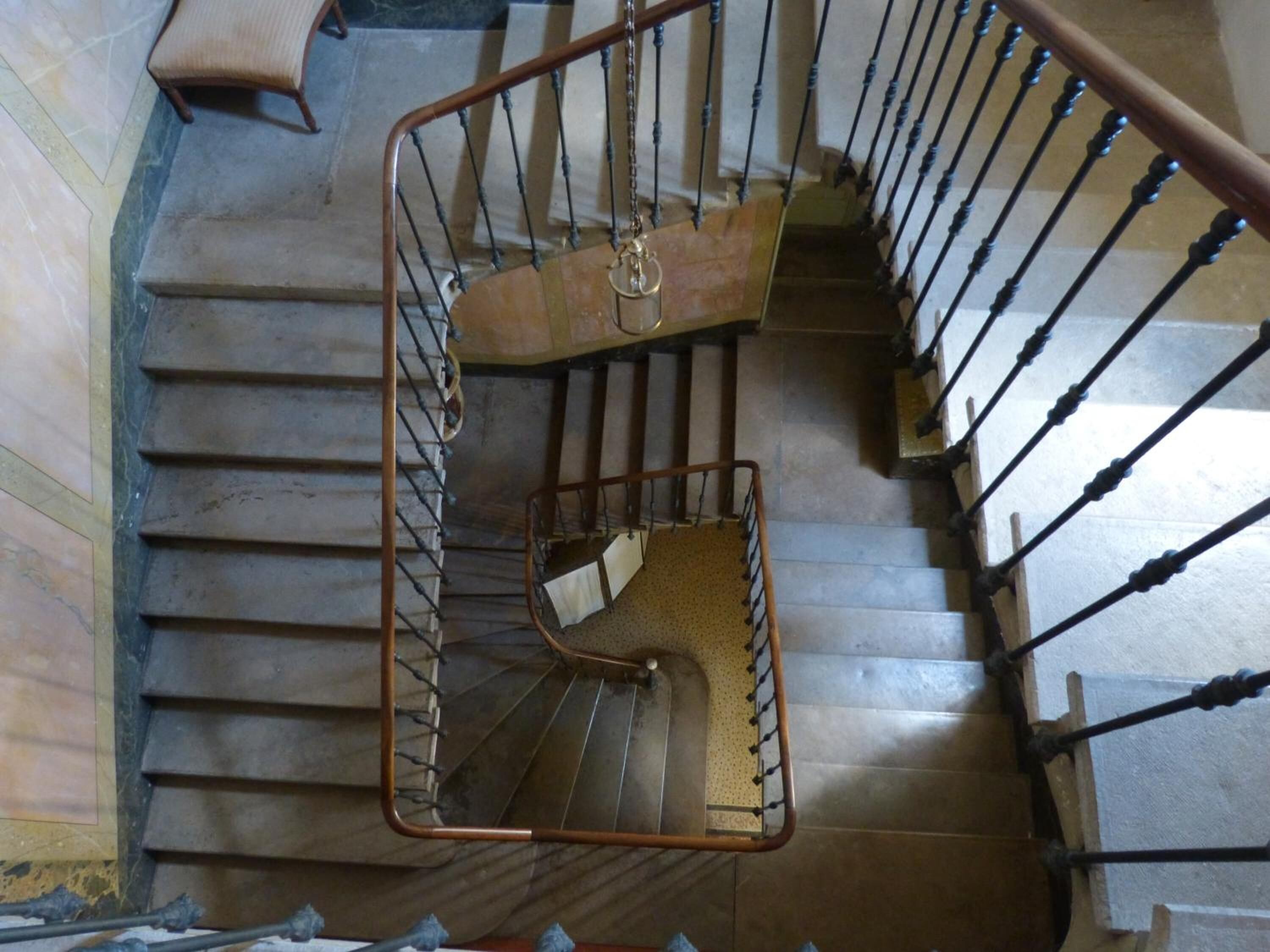 A spiral staircase with a metal handrail and a wooden handrail, leading to an upper floor.