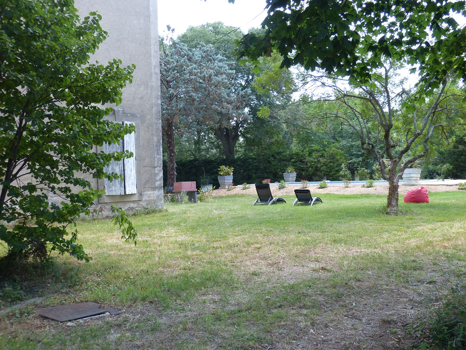 Un espacio al aire libre con césped, dos sillones de descanso, un banco de piedra y un árbol pequeño.