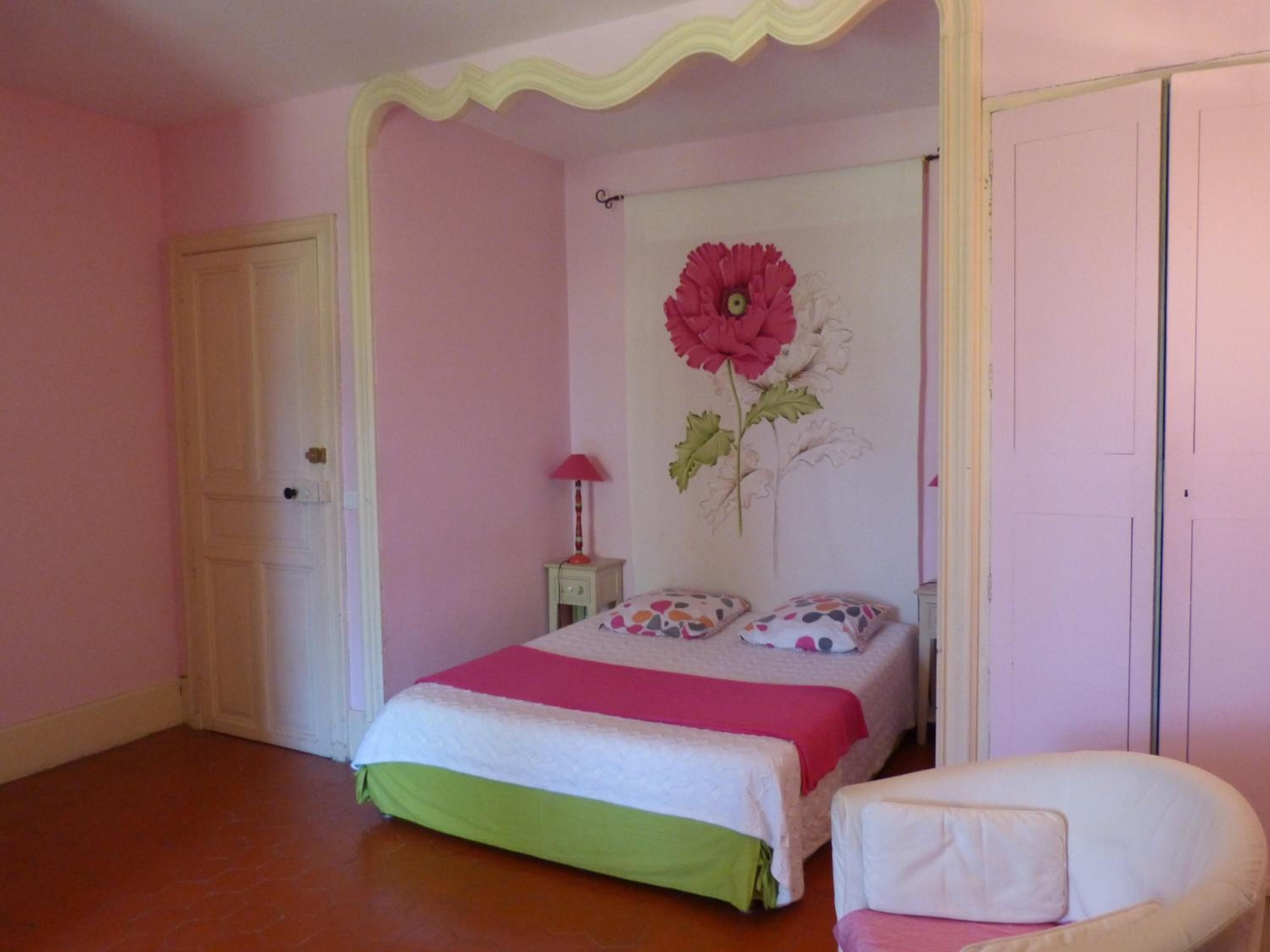 Une chambre à coucher avec un lit, une chaise, une porte et un mur orné d’un tableau représentant des fleurs.