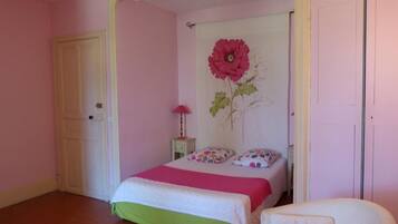 Une chambre à coucher avec un lit, une chaise, une porte et un mur orné d’un tableau représentant des fleurs.