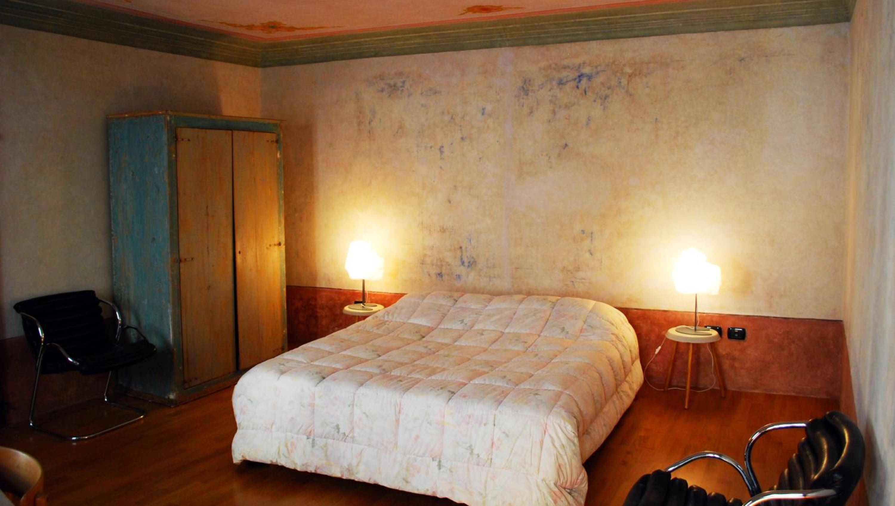 Una habitación de hotel con una cama, dos lámparas de noche, un armario de madera y una silla.
