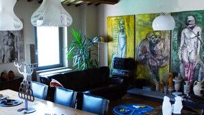 A dining area with a wooden table and chairs, a black sofa, and a painting on the wall. - B&B Camera con Vista (Fossombrone)