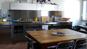 A modern kitchen with stainless steel appliances, a wooden dining table, and a hanging light fixture. - B&B Camera con Vista (Fossombrone)