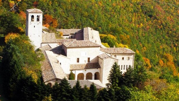 A historic building with multiple levels, arched windows, and a bell tower, surrounded by dense foliage and autumn-colored trees. - B&B Camera con Vista (Fossombrone)