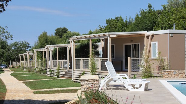 A row of single-story cabins with outdoor seating and a pool. - Mobile Homes Peskera (Medulin)