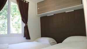 A hotel room with two beds, a window with curtains, and a wooden headboard. - Mobile Homes Peskera (Medulin)