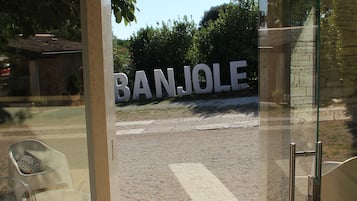 Entrada de un edificio moderno con vista despejada a la calle y un cartel grande que dice "BANJOLE".