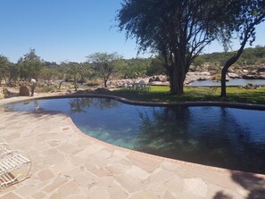 A swimming pool with stone tiles and a view of a natural landscape. - Nyangombe Safari Lodge (Kwekwe)